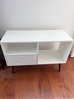 Front view of the white shelf unit showing the top surface, drawer on the left, and open right shelf.