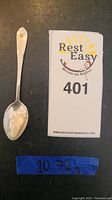 Full view of sterling silver spoon next to lot number card