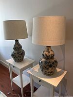 Two floral patterned ceramic table lamps with beige fabric shades placed on small white tables.