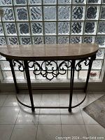 Side view of marble top and steel frame with scrollwork and crescent shape