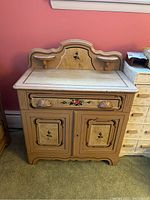 Front view of the antique washstand showcasing the painted floral details on the drawer and cabinet doors along with the decorative back panel and small shelves.