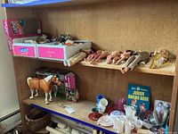 Shelving with multiple toys including boxed Ken toys, loose dolls, horse toy, tea set items, and baking book