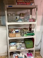 Photo showing shelving unit with glass canisters, jars, some paper and plastic goods on shelves, and tin basket with items on middle shelf.