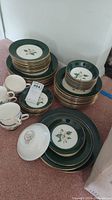 Full set stacked showing various plates, bowls, and cups with floral design and green/gold trim