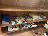 Photo of various cookbooks arranged on a wooden shelf, showing multiple small stacks.
