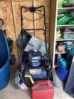 Front view of the Craftsman push lawn mower with grass catch bag, gas can, and fuel stabilizer included, showing condition and setup inside a shed.