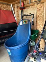 Craftsman electric edger, blue garden bucket with wheels, and green lawn spreader in a barn shed environment