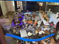 Wide view of the collection on a glass table showing various figurines in ceramic, metal, plastic and glass, including animals, angels, and small decorative items.