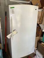 Front view of white upright freezer showing door, handle, dents and stickers