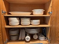 Door cabinet filled with dinnerware including bowls, plates, cups and a metal rack showing organized setup