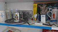 Shelf with various Masonic steins, glass goblets, metal cutter, pen, and metal tray.