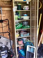 Shelf with multiple ceramic and plastic flower pots and planters, some with dirt and chips, bags of lawn food on middle shelf, garden watering cans on bottom shelves.