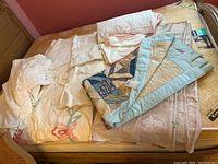 Overview of seven vintage quilts and bedspreads laid on a mattress, showing various sizes, colors, and textile styles including chenille and patchwork.