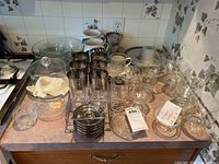 Photo showing multiple glass and stoneware items on a kitchen counter including shrimp cocktail glasses, coasters in metal caddy, clear glass plates, and Salem stoneware shrimp cocktail containers.