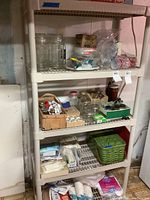 Full front view of the beige plastic shelving unit with four shelves containing various household and pantry items (not included). Unit shows slight discoloration and dust.