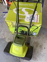 Front view of the green Sunjoe electric tiller, includes handle and guard up top, placed on the box with visible Sunjoe logo.