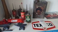 Photo showing several vintage oil cans including Texaco Home Lubricant cans and a Mobil branded red toy truck alongside two small anvil-shaped metal tools.