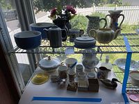 Wide view of multiple vintage china items displayed on shelves including bowls, pitchers, teapots, cups, and decorative ceramics.