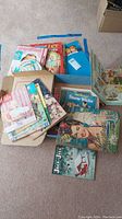 Overview of various paper doll and vintage children's books spread on the floor with visible titles and colorful vintage illustrations.