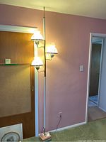 Full view of the vintage pole light standing in a room, showing all three glass shades lit.