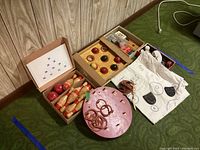 Wide view of vintage wooden toys including bowling set, ball toss, ring toss, yo-yos, playing cards, canvas bag, and coin toss components
