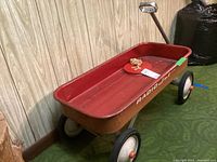 Side view of vintage Radio Flyer wagon showing red metal bed, handle, and some rust.