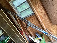 View of 3 metal wash line poles leaning against wall with other garden tools including rakes and shovels