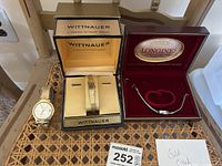 Three watches displayed: men's and ladies' Wittnauer watches with original box and Longines watch in red velvet box on wicker table