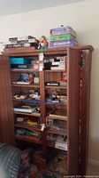 Open view of the cabinet showing multiple shelves filled with assorted board games, puzzles, and a Mr. Potato Head toy on top.