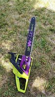 Full view of Poulan Wild Thing 18" chain saw laying on grass, showing yellow and purple color scheme and chain bar.
