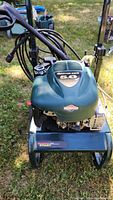 Close-up photo of Briggs & Stratton Quantum Gold 5.0 HP pressure washer engine mounted on green and black frame with wheels, visible fuel cap, and hoses.