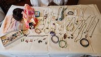 Full layout of assorted costume jewelry including necklaces, bracelets, earrings, and scarfs on a flat white surface