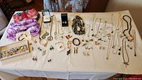 Full display of assorted costume jewelry on table including necklaces, earrings, rings, and bracelets along with two folded scarfs