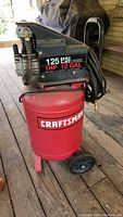 Red Craftsman air compressor tank with black motor, 125 PSI max, 1 HP, 12 gallon, mounted on wheels.