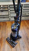 Full view of Dyson Ball Animal DC25 upright vacuum cleaner showing entire unit including handle, dust bin, ball base, and brush head attachment on hardwood floor.