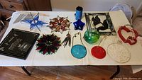 Table display of various stained glass ornaments, glass balls, metal wind chimes and fabric or woven hanging decorations.