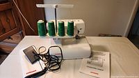 Janome Cover Pro 1000CP sewing machine with multiple green spools on thread holder, foot pedal, and Janome fabric cover on table.
