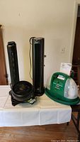 Photo of four appliances on a table including two black towers (heater and air purifier), black round fan, and green-white Bissell cleaner