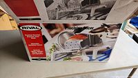 Box showing Rival brand and product image of Precision Slicer with serrated stainless steel blade and adjustable thickness control.