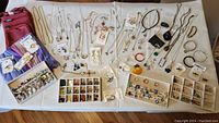 Wide view of all jewelry pieces laid out on a white cloth, including the purple scarf and red leather bag, multiple necklaces, earrings, rings, and bracelets.