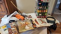 View of the assortment of crafting books, wooden knitting needles, and stacked clear plastic storage boxes with colorful threads.