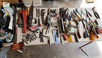 Wide view of all tools and accessories laid out on a table including wrenches, pliers, screwdrivers, drill bits, hand saw, and a leather pouch.