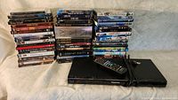 Stacked DVDs and Blu-rays with Panasonic Blu-ray player and remote in front on beige cloth surface