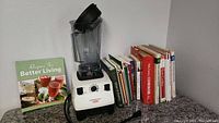 Vitamix blender with container, lid, and several cookbooks on countertop.