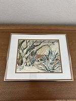Full image of framed watercolor desert landscape painting on wood surface.