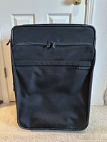 Front view of the black Briggs & Riley suitcase showing dual zipper pulls and brand logo tag on front pocket.
