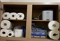 Photo of bathroom cabinet interior showing bath tissue rolls and electronic device
