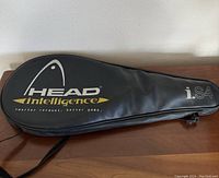 Black Head Intelligence i.S4 tennis racquet case lying flat on a wooden surface with large white and yellow graphics.