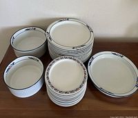 Overview of the entire dinnerware lot including stacked plates and deep dishes on a wooden surface.