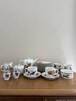 Full lot overview showing teapot, creamer, sugar bowl, salt and pepper shakers, plates, cups, saucers, and small covered dish all with colorful fruit and leaf designs typical of the Evesham Collection.